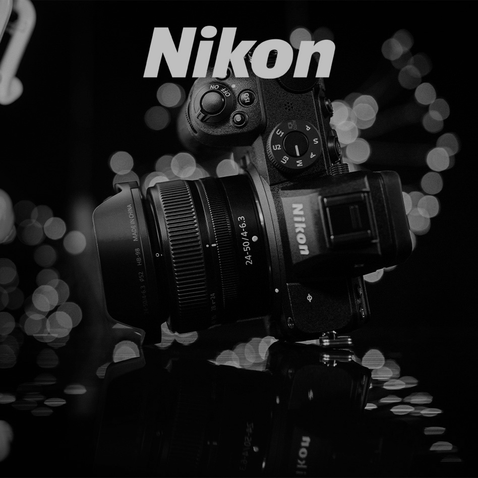 Fotoaparát Nikon s objektívom 24-50 mm na lesklom povrchu s rozostrenými svetlami v pozadí