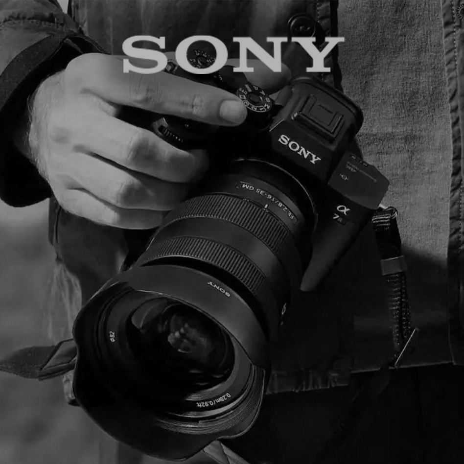 Čiernobiely záber ruky, ktorá drží fotoaparát Sony so širokouhlým objektívom