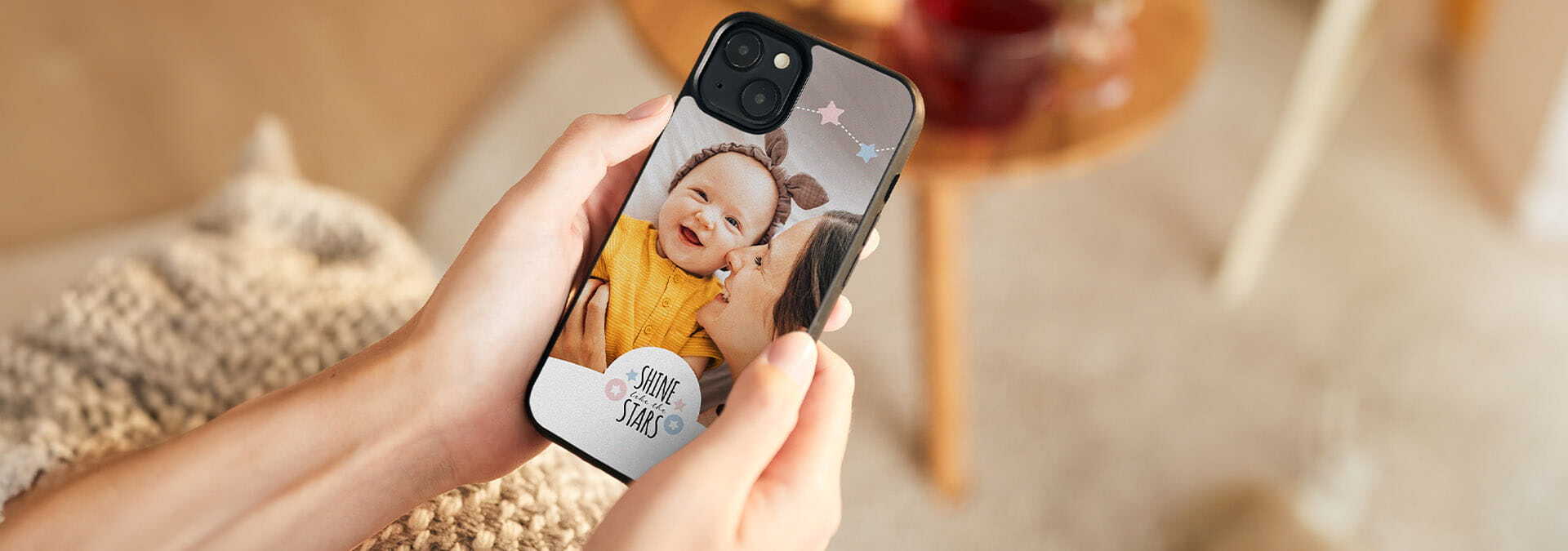 Osoba drží mobilný telefón s obalom zdobeným fotkou a nápisom „Shine like the stars“