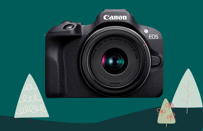 Čierny fotoaparát Canon EOS na tmavozelenom pozadí s vianočnými stromčekmi vľavo a vpravo