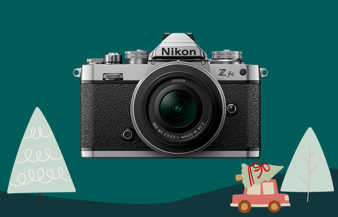 Kamera Nikon Z fc na tmavozelenom pozadí s vianočnými motívmi, stromčekmi a autíčkom s darčekom